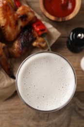 Photo of Glass of beer, delicious baked chicken wings and sauce on wooden table, closeup