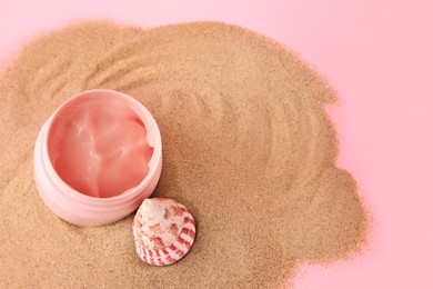 Photo of Open jar of cream and seashell on sand against pink background, above view. Space for text