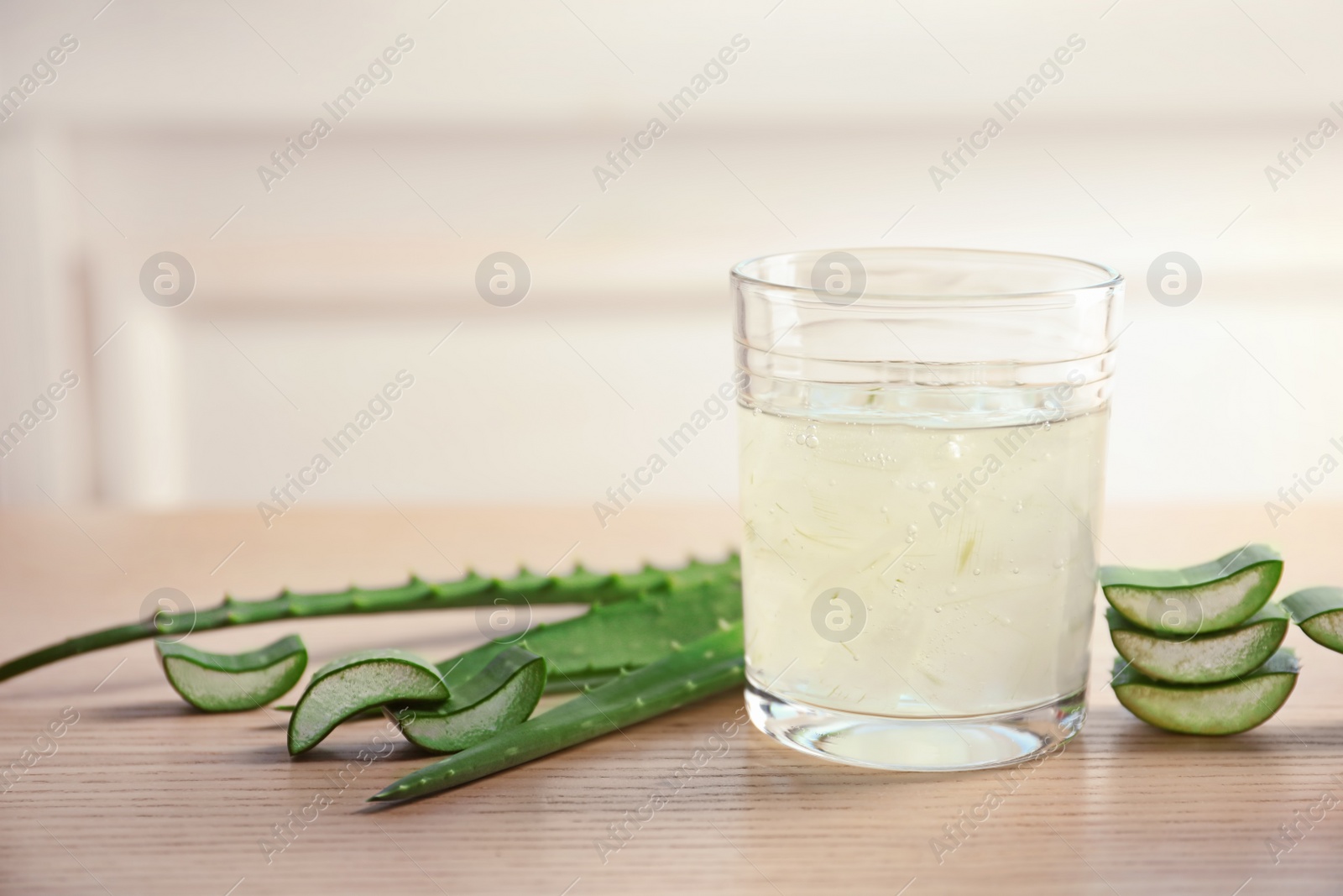 Photo of Glass of aloe vera juice and green leaves on wooden table against light background with space for text