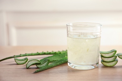 Photo of Glass of aloe vera juice and green leaves on wooden table against light background with space for text