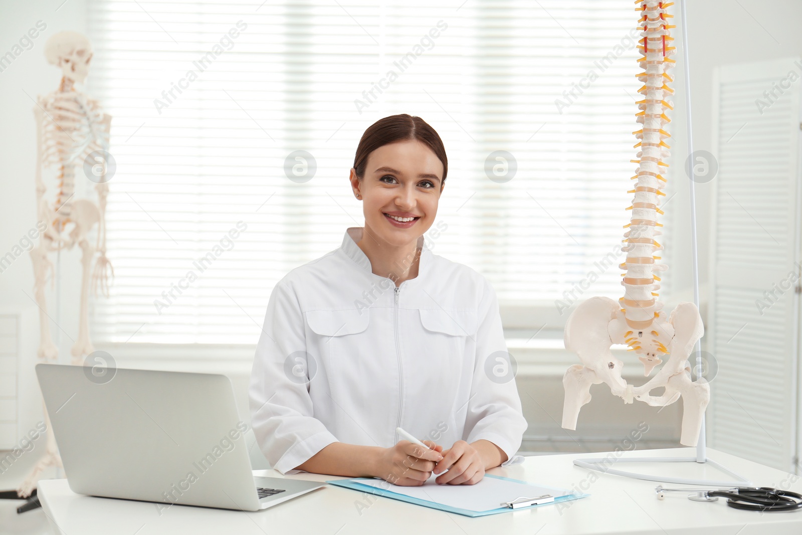 Photo of Female orthopedist with laptop near human spine model in office