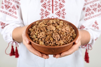 Photo of Woman in slavic shirt holding bowl with traditional kutia, closeup