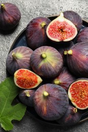 Photo of Whole and cut ripe figs with leaf on light grey textured table, flat lay