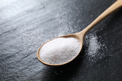 Photo of Organic white salt in spoon on black table, closeup