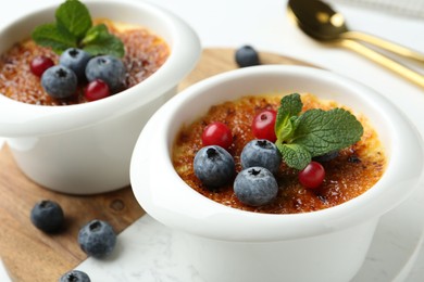 Photo of Delicious creme brulee with berries and mint in bowls on table, closeup