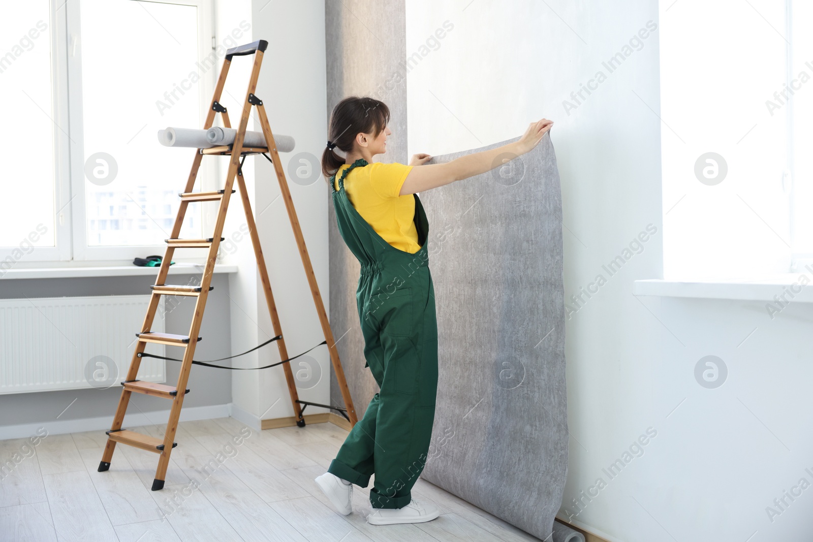 Photo of Woman hanging stylish gray wallpaper in room