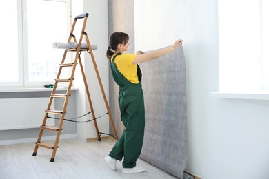 Woman hanging stylish gray wallpaper in room