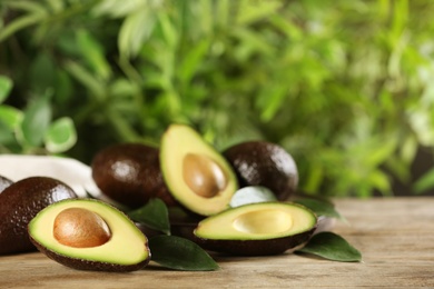 Photo of Whole and cut avocados with green leaves on wooden table