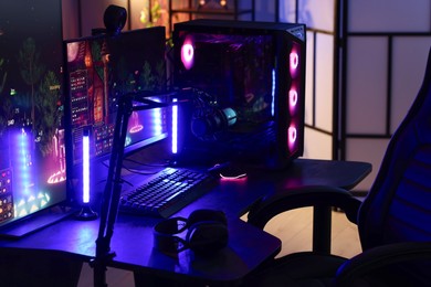 Photo of Playing video games. Stylish room interior with modern computer and gaming chair in neon lights