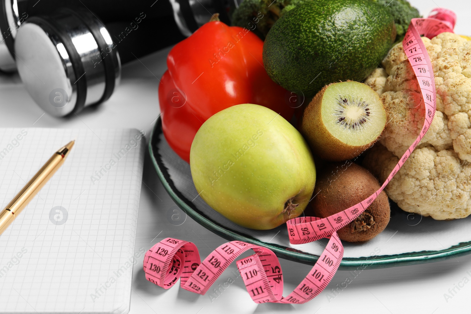 Photo of Healthy diet. Plate with products, measuring tape and notebook on white wooden table, closeup