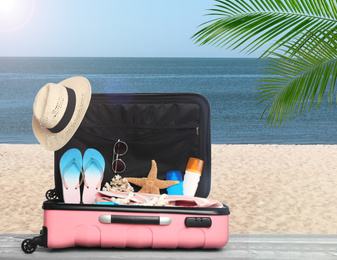 Image of Suitcase with different beach objects on grey wooden table near sea