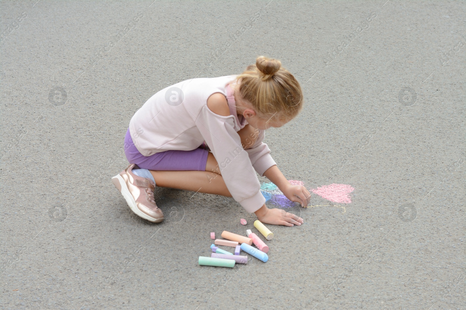 Photo of Little child drawing butterfly and heart with chalk on asphalt