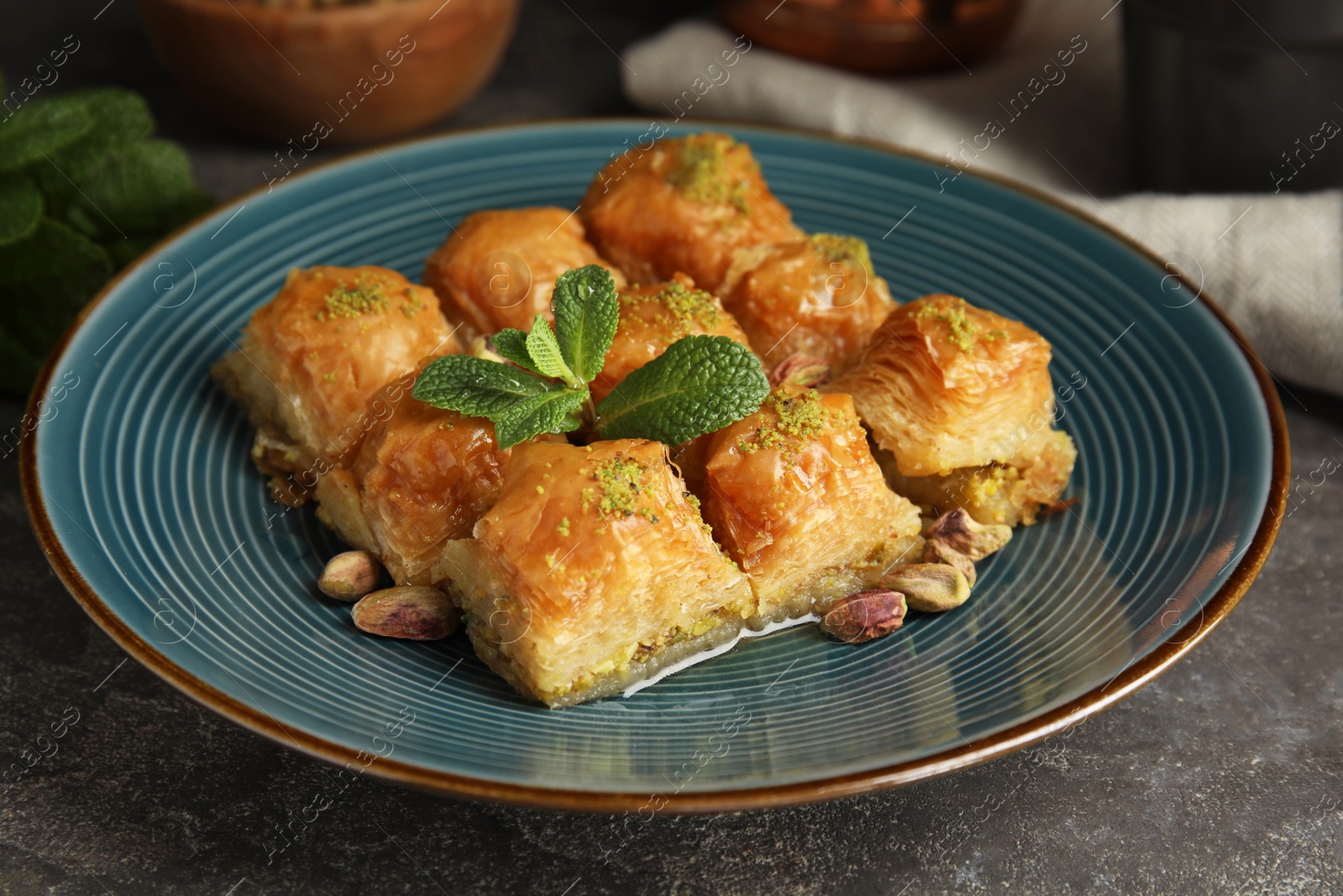 Photo of Delicious baklava with pistachio nuts and mint on grey table