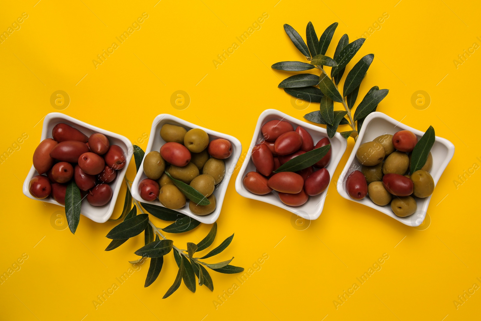 Photo of Different fresh olives and green leaves on yellow background, flat lay