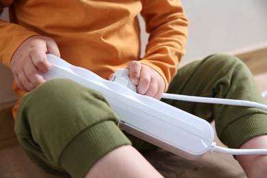 Photo of Little child playing with power strip and plug indoors, closeup