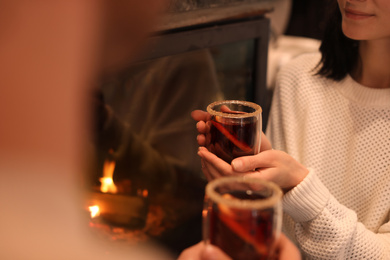 Couple with mulled wine near fireplace indoors, closeup. Winter vacation
