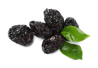 Photo of Heap of sweet dried prunes and green leaves on white background, top view