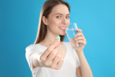 Photo of Young woman with glass of water and vitamin pill against blue background, focus on hand