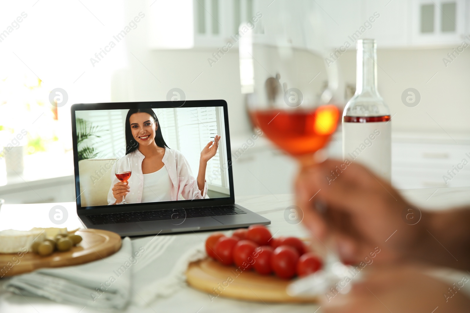 Photo of Friends drinking wine while communicating through online video conference in kitchen. Social distancing during coronavirus pandemic