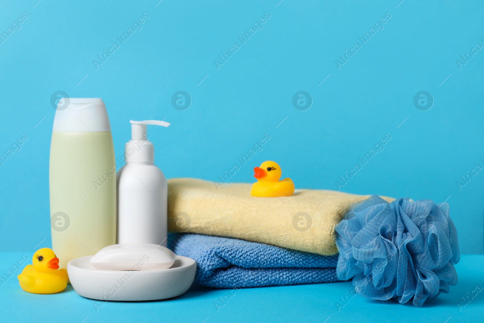 Photo of Baby cosmetic products, bath ducks, sponge and towels on light blue background