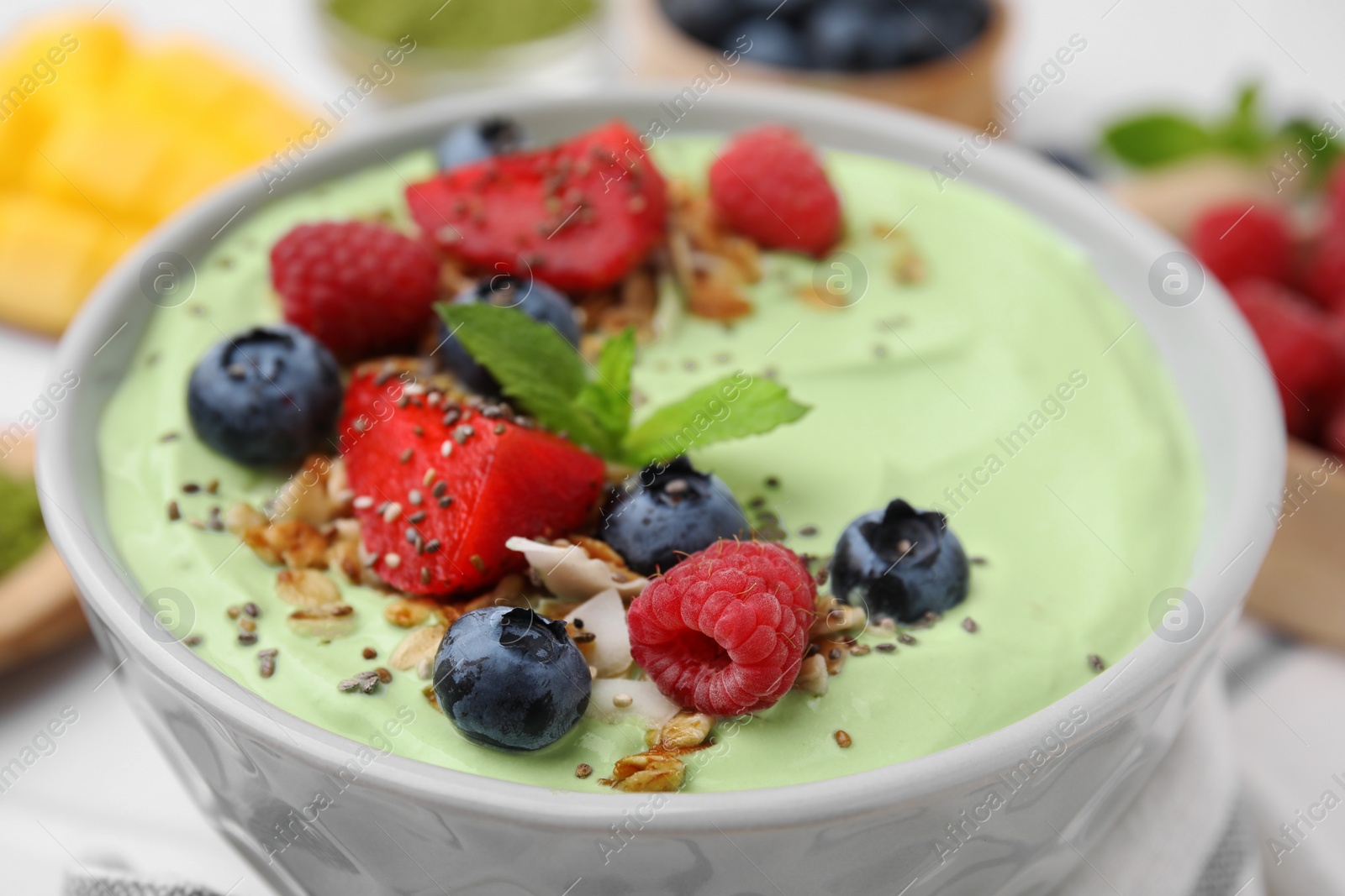 Photo of Tasty matcha smoothie bowl served with berries and oatmeal on table, closeup. Healthy breakfast