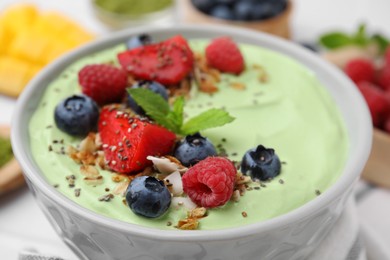 Tasty matcha smoothie bowl served with berries and oatmeal on table, closeup. Healthy breakfast