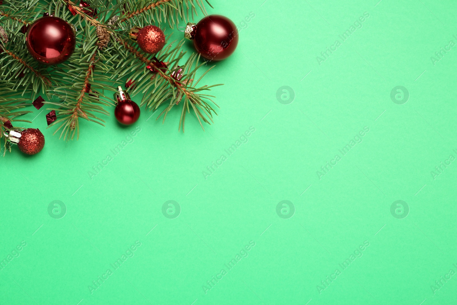 Photo of Fir branch with shiny Christmas balls and confetti on green background, flat lay. Space for text