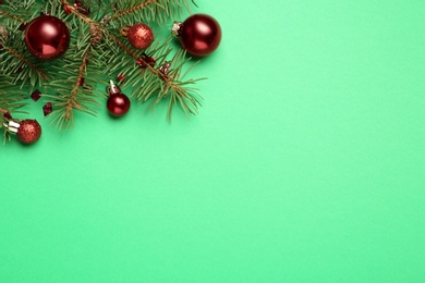 Fir branch with shiny Christmas balls and confetti on green background, flat lay. Space for text