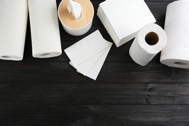 Photo of Clean napkins, box with tissues and rolls of paper towels on wooden table, flat lay. Space for text