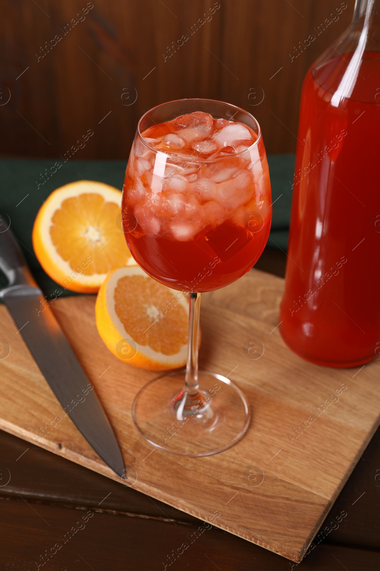 Photo of Aperol spritz cocktail and ice cubes in glass and bottle on wooden table