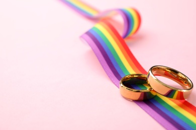 Wedding rings and rainbow ribbon on color background, space for text. Gay symbol