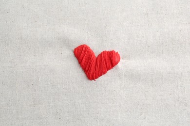 Photo of Embroidered red heart on light cloth, top view