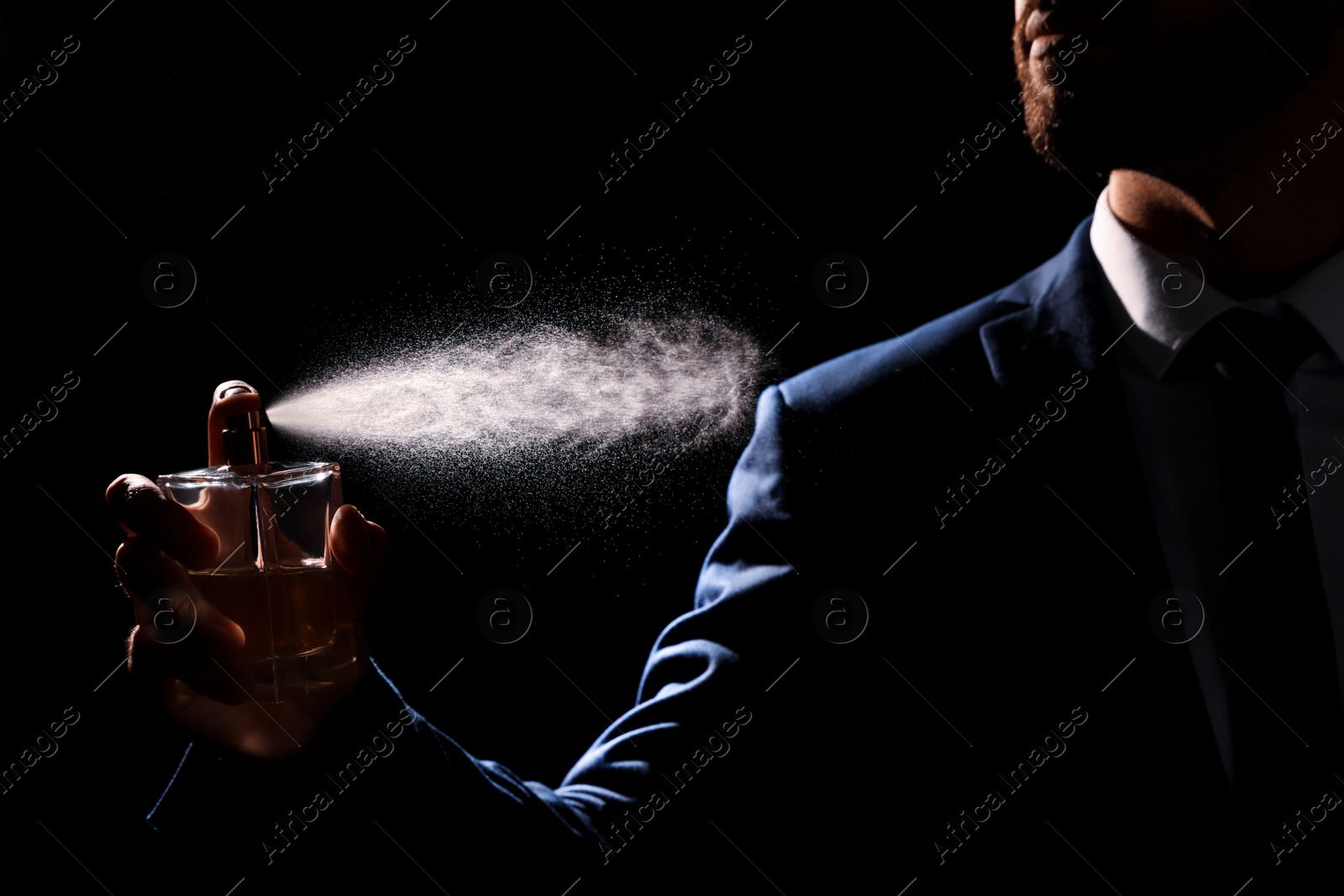 Photo of Man spraying luxury perfume on black background, closeup