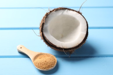 Photo of Spoon with coconut sugar and half of fruit on light blue wooden table, closeup