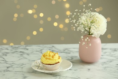 Delicious cupcake with yellow cream and flowers on white marble table against blurred lights