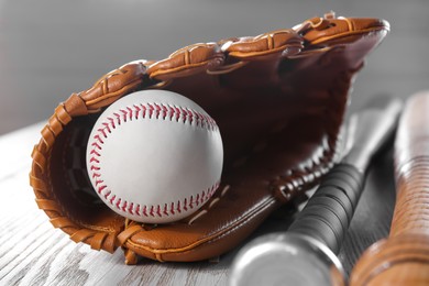 Baseball glove, bats and ball on white wooden table, closeup