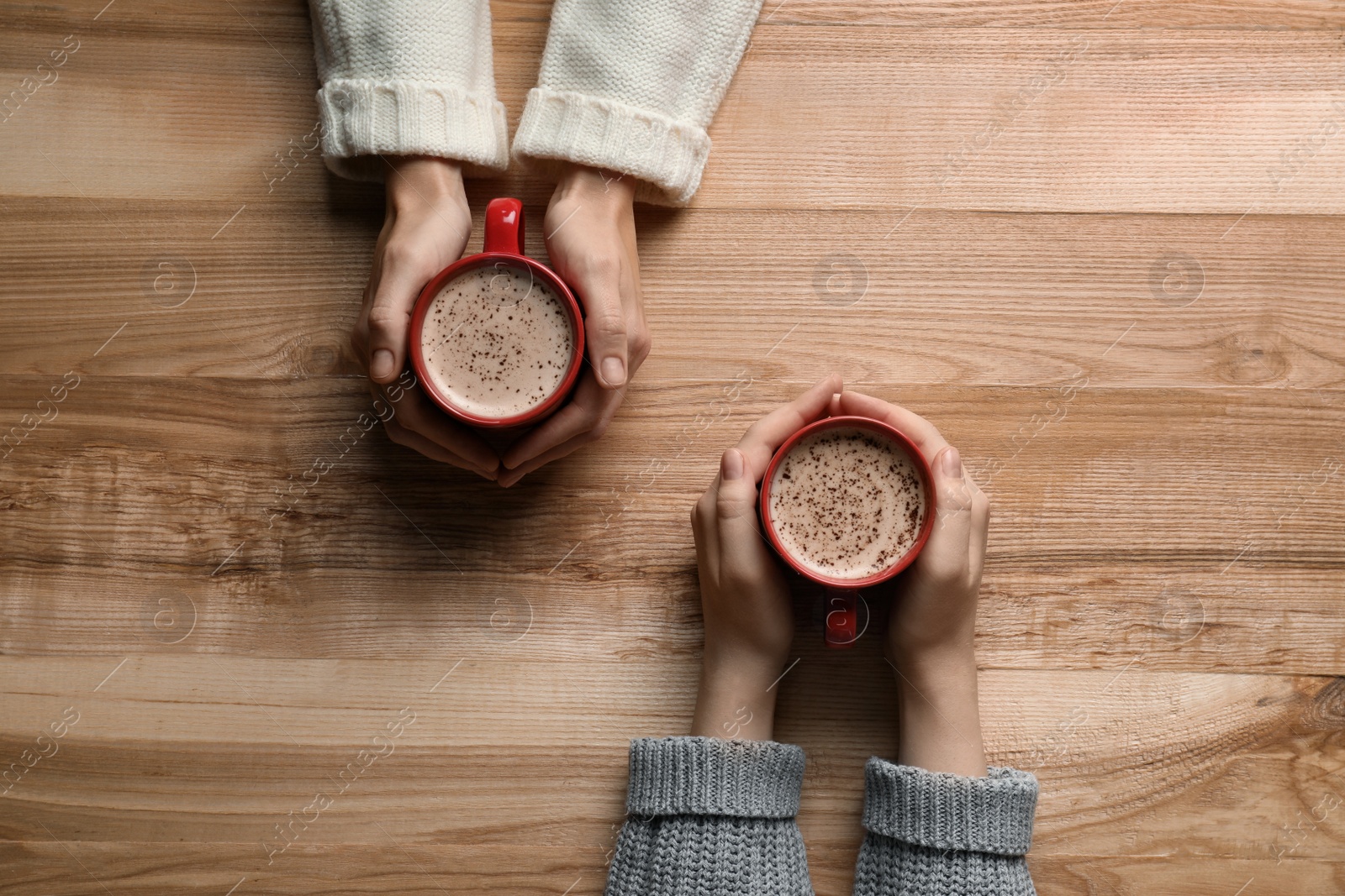 Photo of Women with cups of coffee at wooden table, top view