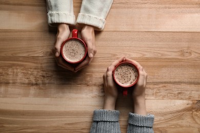 Women with cups of coffee at wooden table, top view