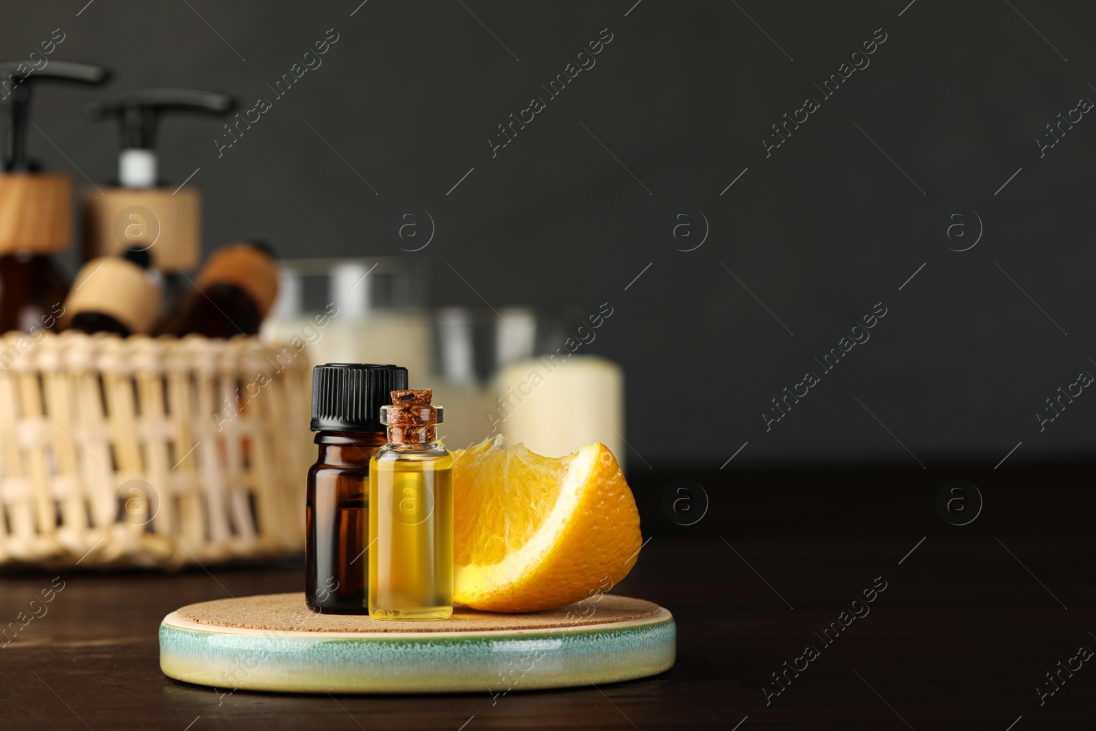 Photo of Bottles of essential oil and orange on wooden table, space for text