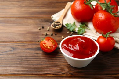 Photo of Delicious ketchup in bowl and tomatoes on wooden table. Space for text