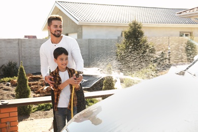 Photo of Dad and son washing car at backyard on sunny day