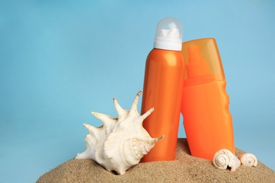 Sand with bottles of sunscreens and seashells against light blue background, space for text. Sun protection