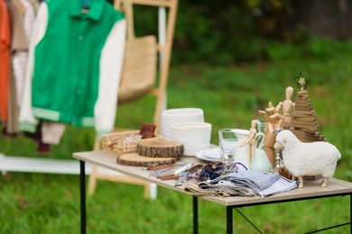 Photo of Clothing rack and small table with different items outdoors. Garage sale