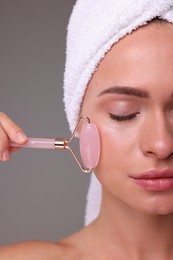 Photo of Young woman massaging her face with rose quartz roller on grey background, closeup