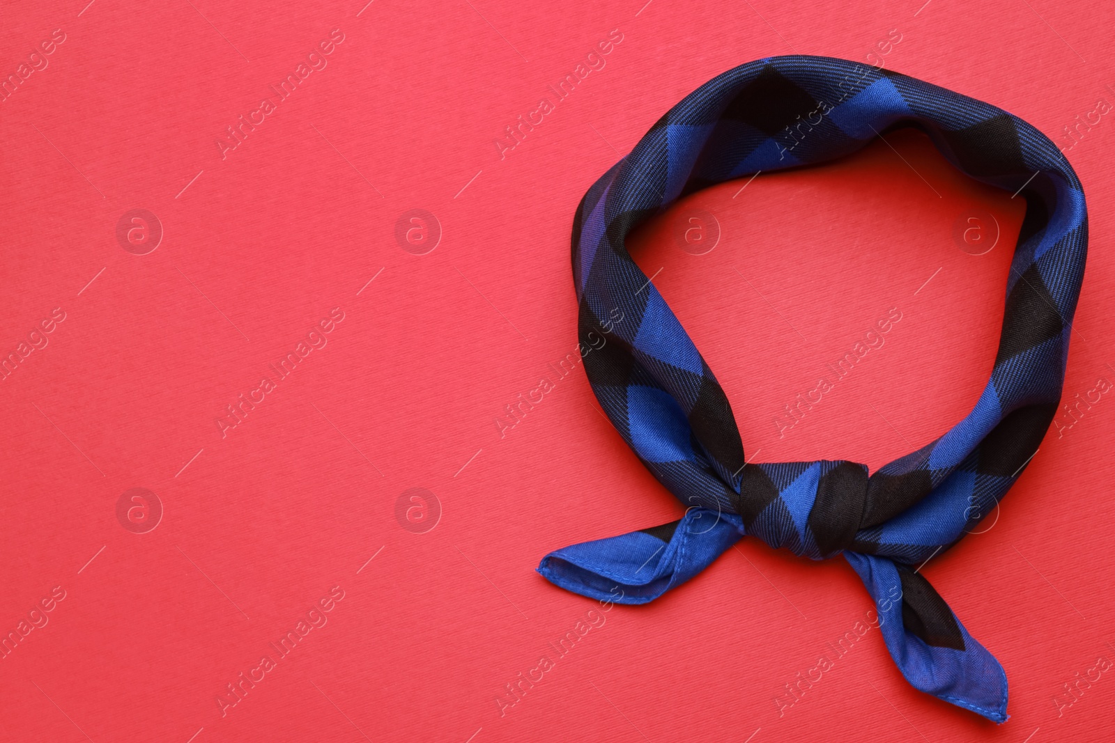 Photo of Tied blue bandana with check pattern on red background, top view. Space for text