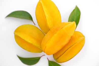 Delicious ripe carambolas with green leaves on white background, top view