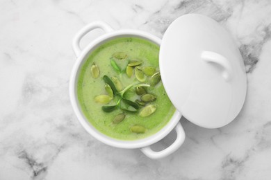 Delicious broccoli cream soup with pumpkin seeds on white marble table, top view