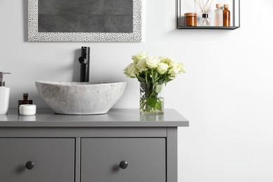 Photo of Vase with beautiful white roses and toiletries near sink in bathroom, space for text