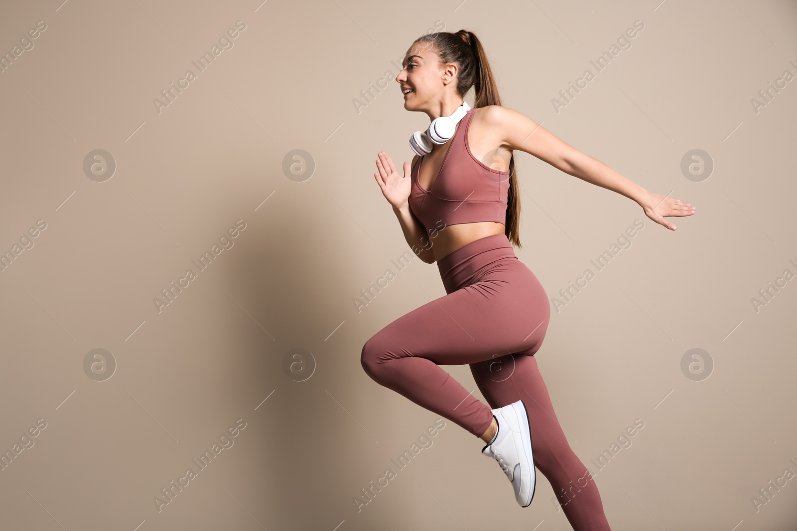 Photo of Young woman in sportswear with headphones running on beige background