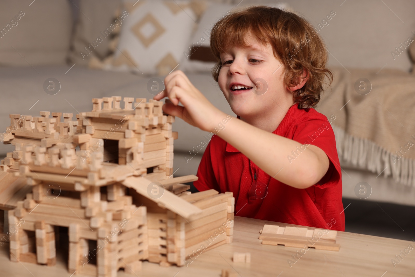 Photo of Cute little boy playing with wooden castle at table in room. Child's toy